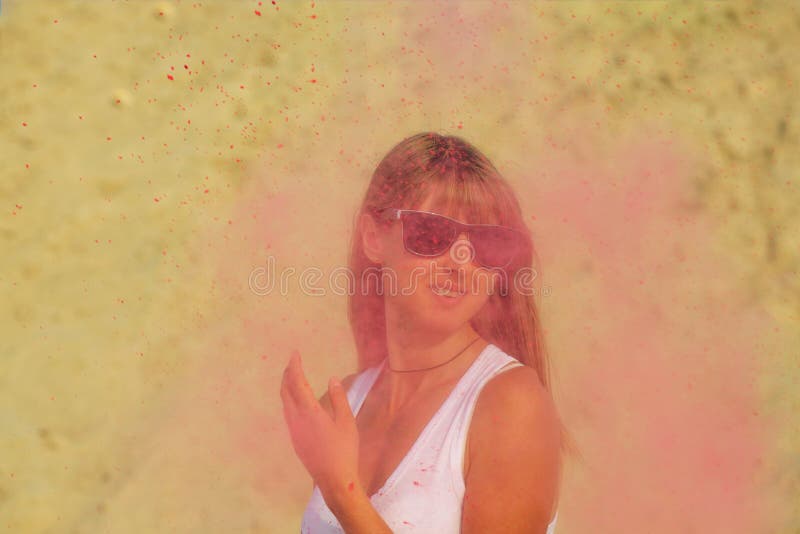 Positive blonde girl in sunglasses playing with colorful dry paint Holi at the desert. Empty space. Positive blonde woman in sunglasses playing with colorful dry royalty free stock photo
